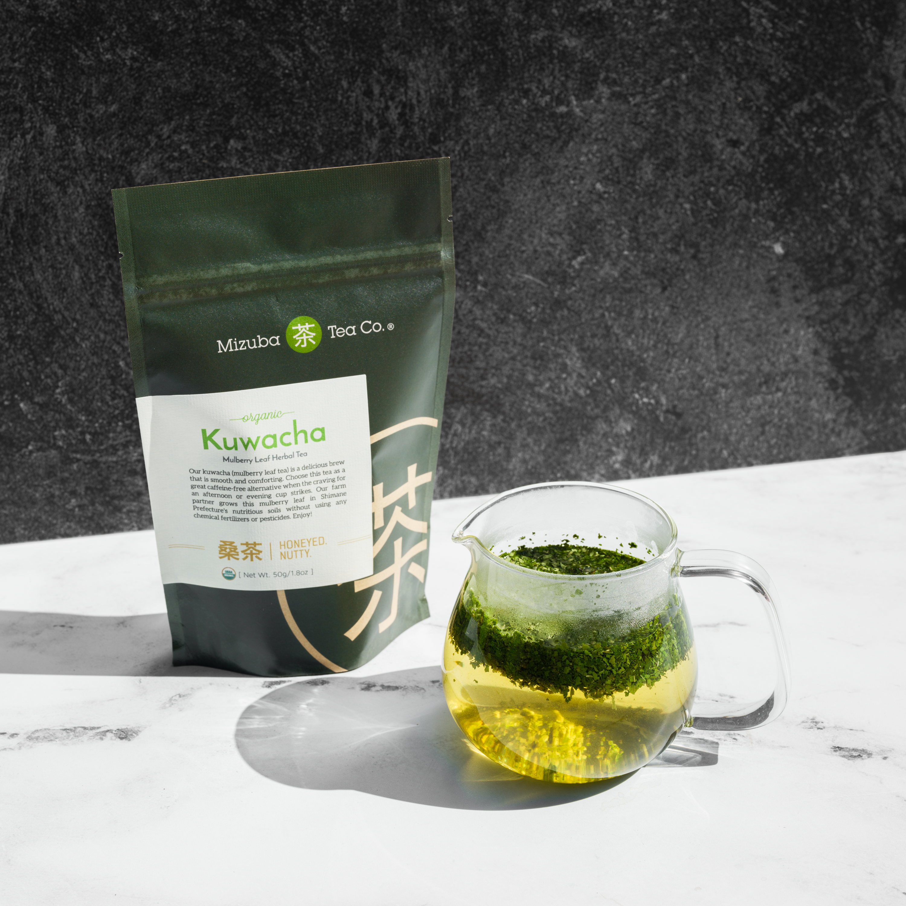 Organic Kuwacha green tea next to a pitcher with steeping tea