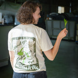 Woman wearing a custom illustrated shirt with Japanese tea design holds a fresh tea leaf from the fields of Japan