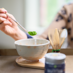 Person scooping  matcha powder into a tea cup