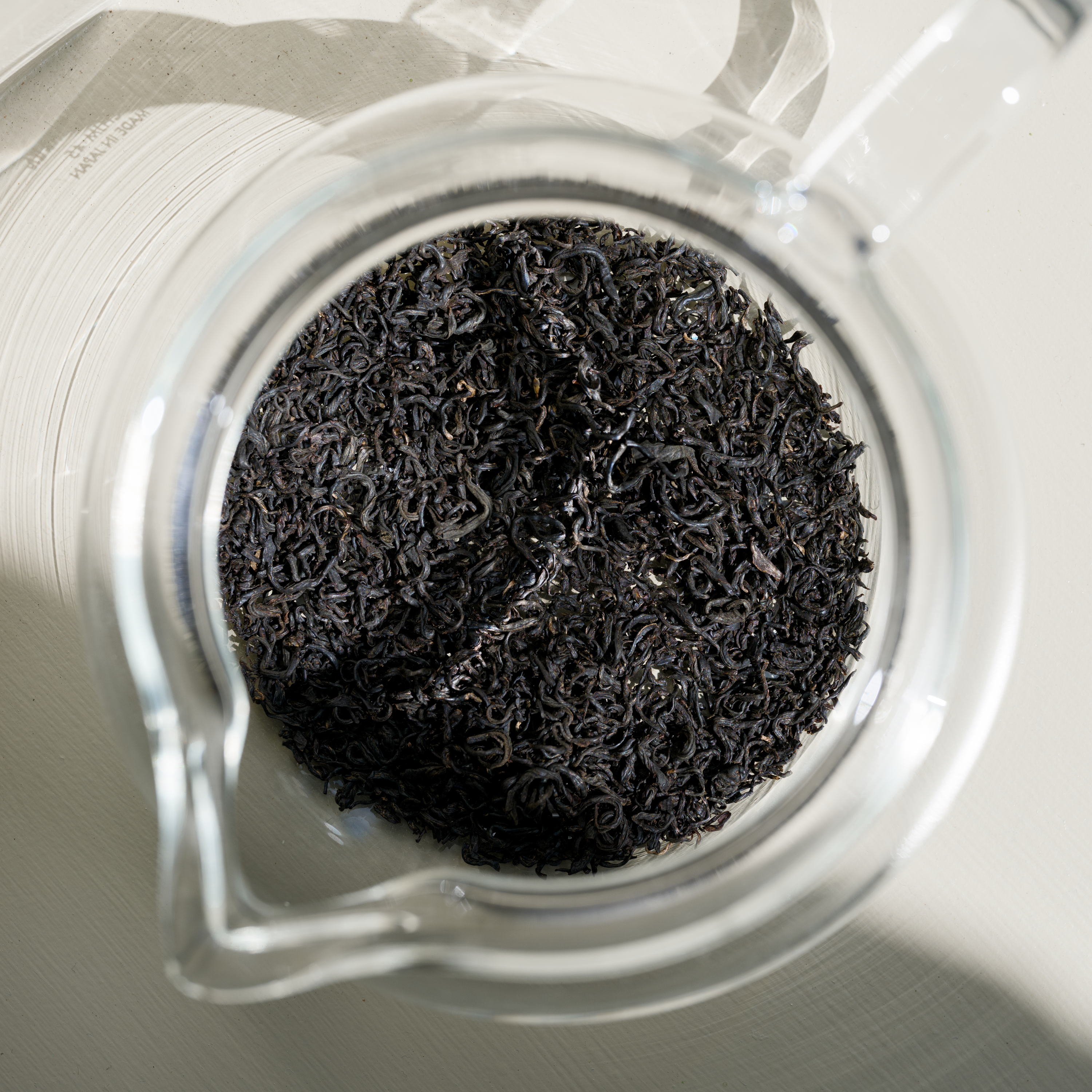 Close-up of Japanese black shincha tea leaves in a glass jar on a white background