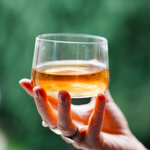 Hand holding a glass of wakoucha Japanese black tea against a blurred green background