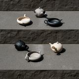 Set of handmade, Japanese Tokoname ceramic teapots and yuzamashi tea tools in beige, black, and grey colors on a stone surface