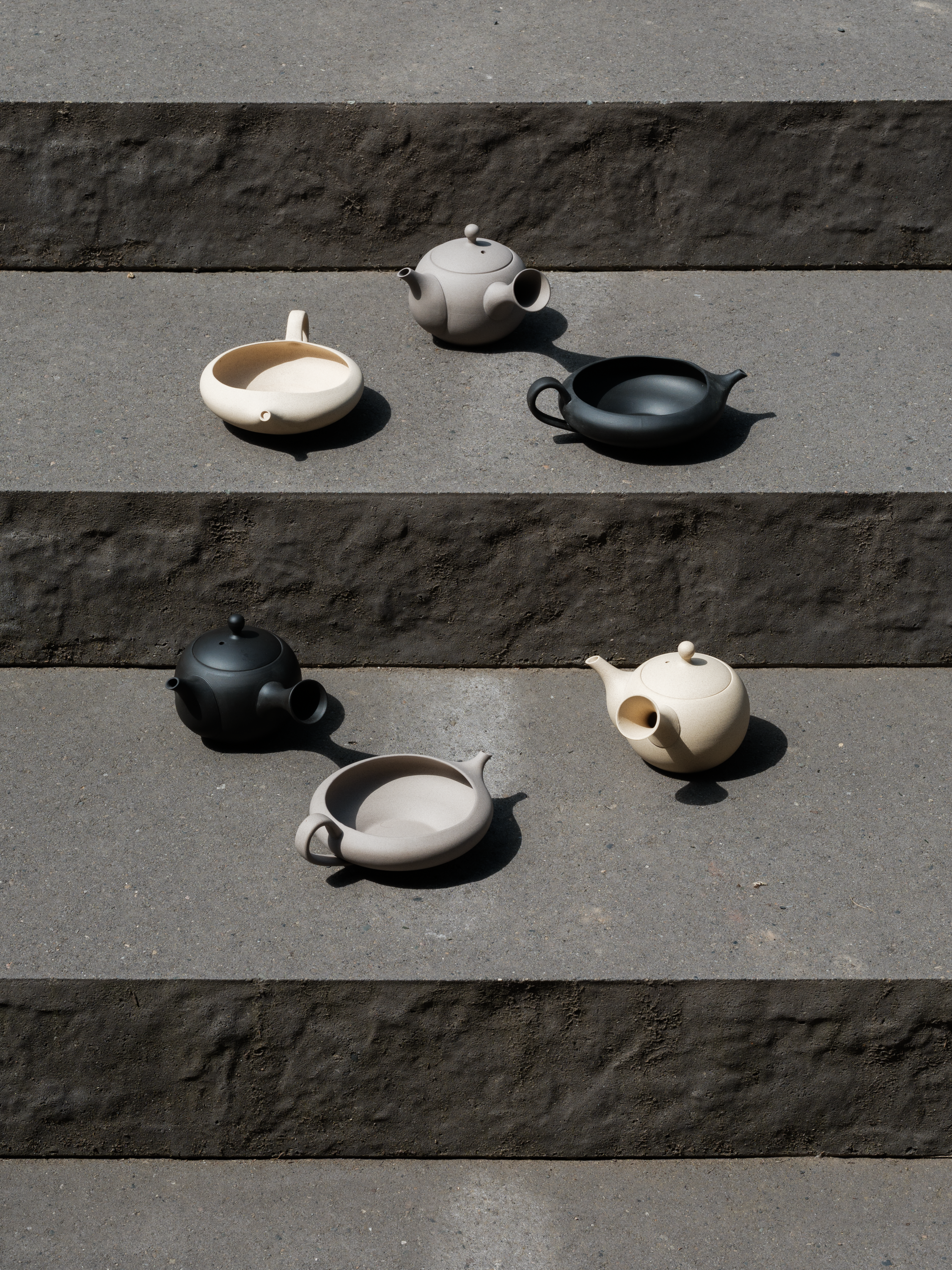 Set of handmade, Japanese Tokoname ceramic teapots and yuzamashi tea tools in beige, black, and grey colors on a stone surface
