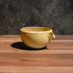Golden yellow ceramic matcha chawan tea bowl on a wooden surface with a dark textured background