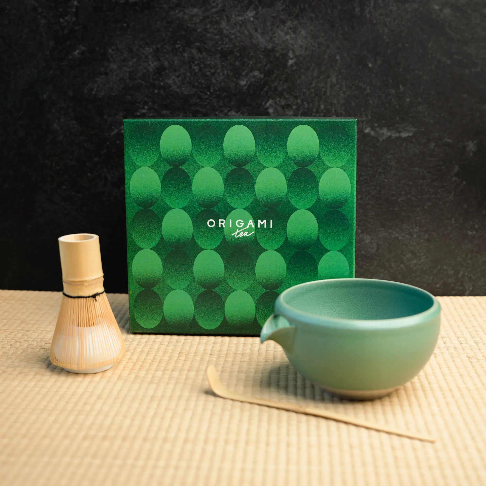A chasen, chawan, and matcha bowl in front of a green box labeled "Origami Tea"