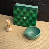 A chasen, chawan, and matcha bowl in front of a green box labeled "Origami Tea"