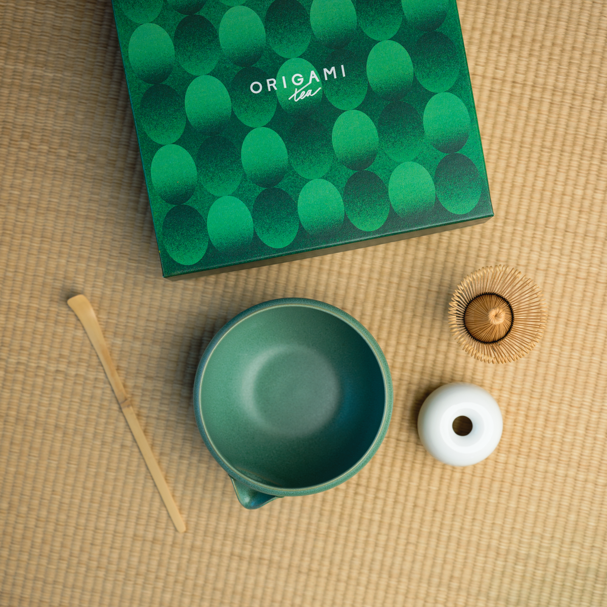 top Down view of a chasen, chawan, and matcha bowl in front of a green box labeled "Origami Tea"