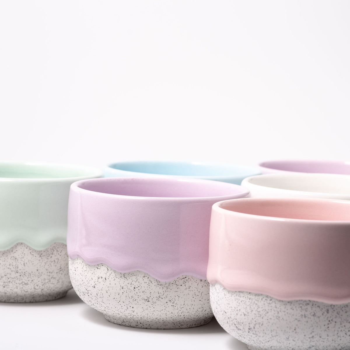 Set of ceramic bowls with speckled base and pastel top in various colors on a white background