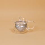 A modern glass teapot sits on a yellow background.