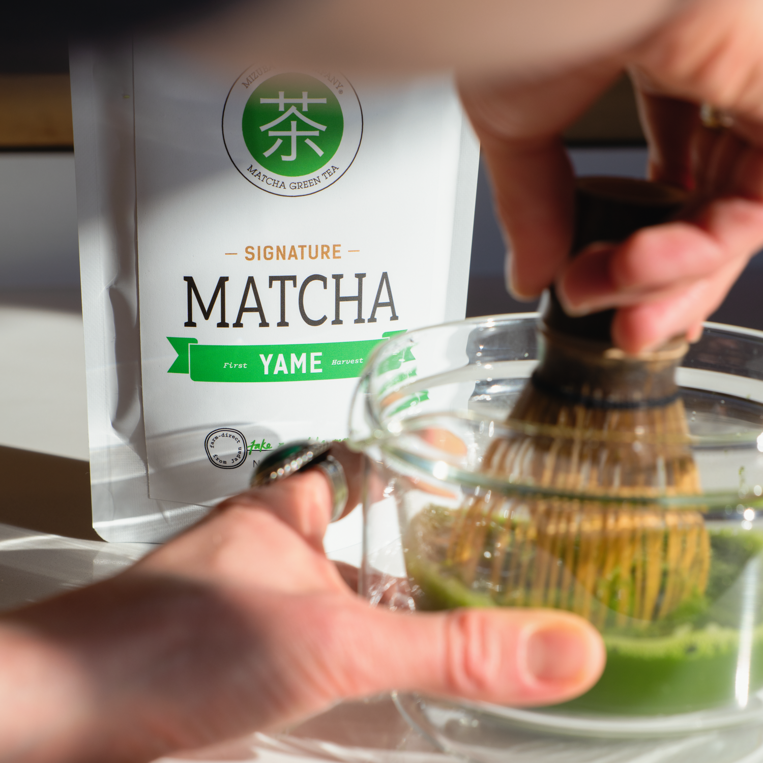Person preparing matcha tea with a package of 'Signature Matcha Yame' in the background.