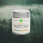 A tin of Mizuba Tea Co. Shirakawa matcha green tea from Japan superimposed on a cloudy forest scene